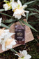 A bar of Harvest Chocolate's Vanilla Bean Sea Salt chocolate placed on a piece of wood surrounded by blooming white daffodils on a garden floor.