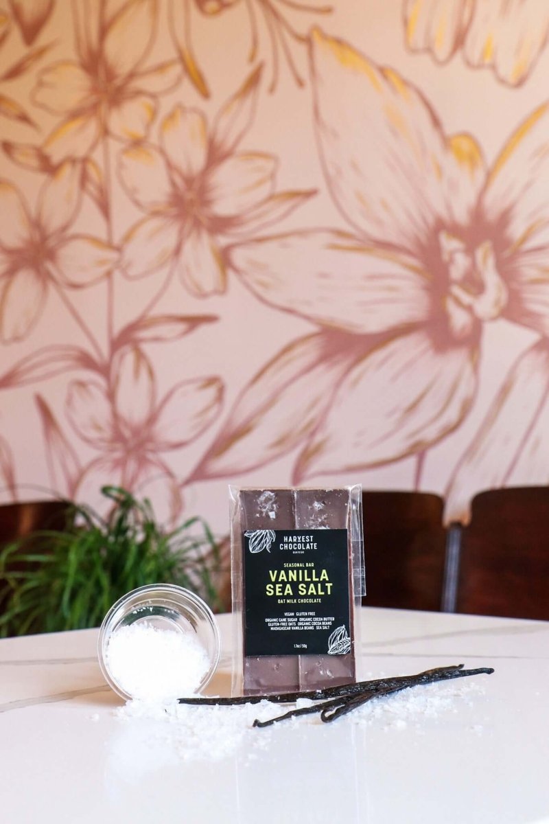 Vanilla Bean Sea Salt dairy free chocolate bar displayed in-store at Harvest Chocolate, with floral mural in background.