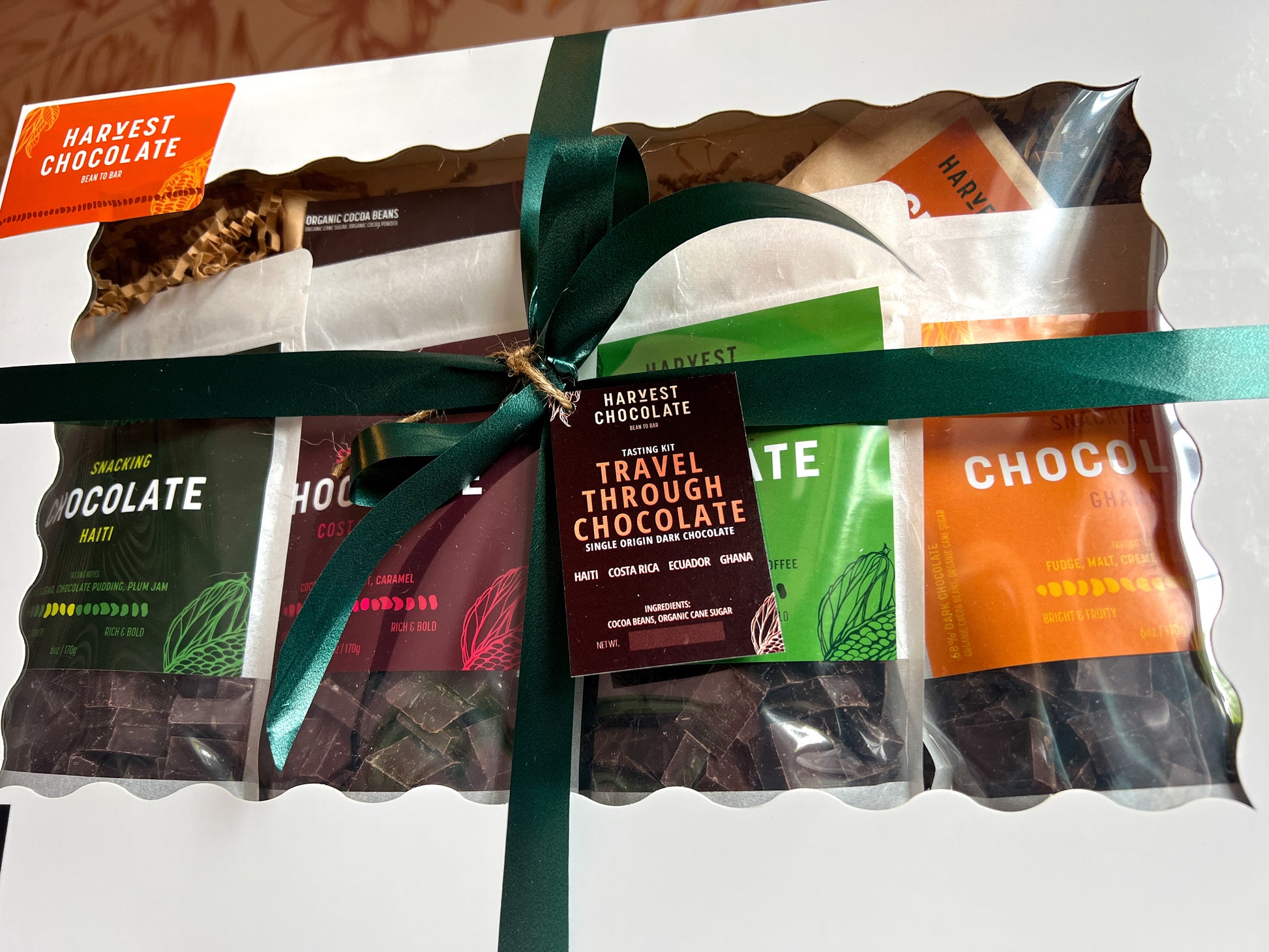 A collection of five Harvest Chocolate Travel Through Chocolate Gift Boxes in colorful wrappers, tied together with a green ribbon and a dried star anise, placed on a marbled surface.