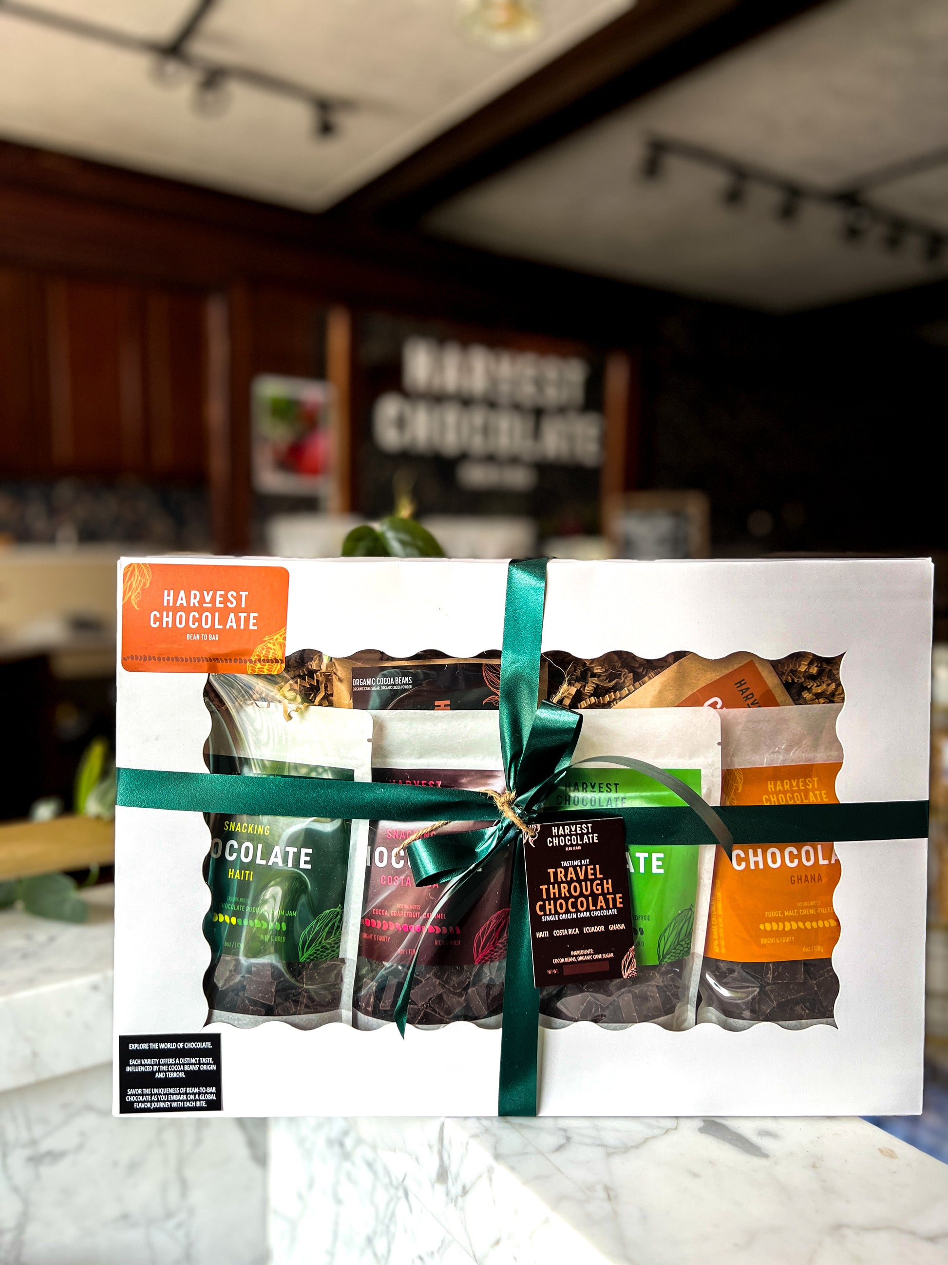 A Travel Through Chocolate Gift Box by Harvest Chocolate, featuring multiple flavors of bean-to-bar chocolate bars, tied with a green ribbon, displayed on a counter in a kitchen setting.