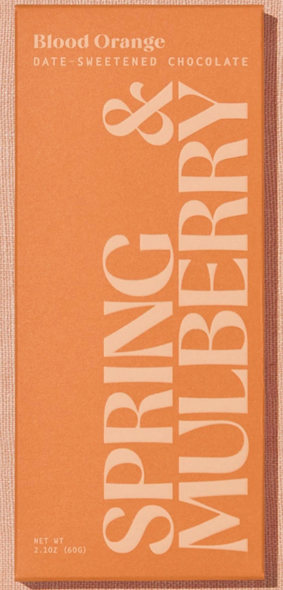 The image features an orange box of Harvest Chocolate's "Blood Orange Date-Sweetened Chocolate," weighing 2.1 oz (60g), with bold, light-colored lettering on the front.